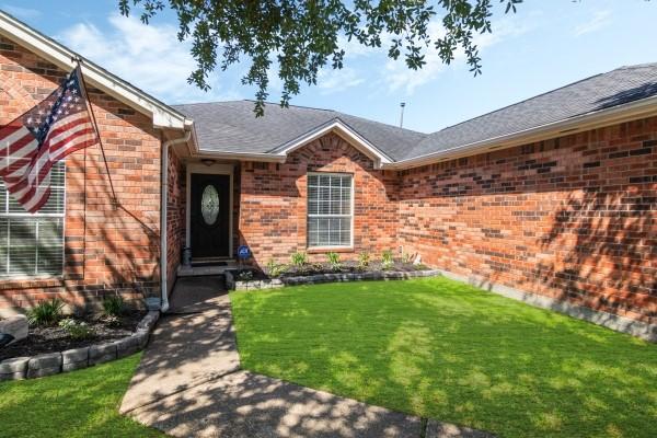 property entrance with a shingled roof, brick siding, and a lawn