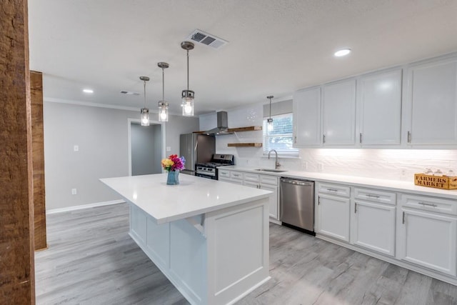kitchen featuring wall chimney range hood, a sink, appliances with stainless steel finishes, visible vents, and a kitchen island