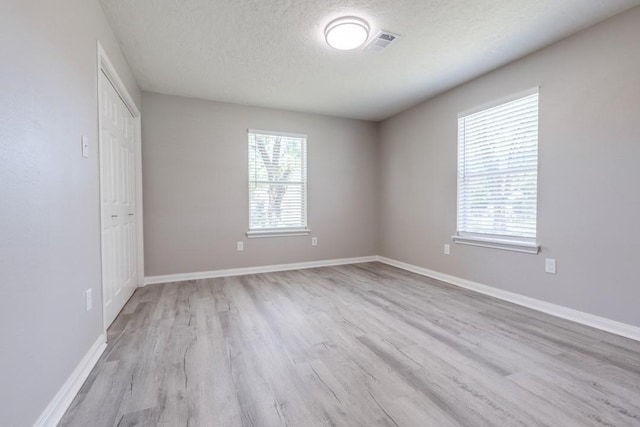 empty room with baseboards, visible vents, a textured ceiling, and light wood finished floors