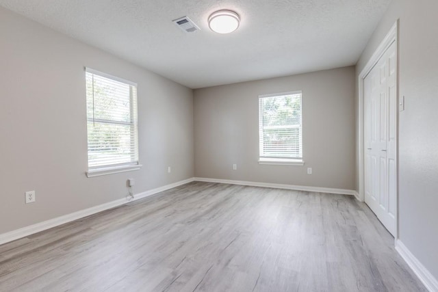unfurnished bedroom with light wood finished floors, a textured ceiling, baseboards, visible vents, and a closet