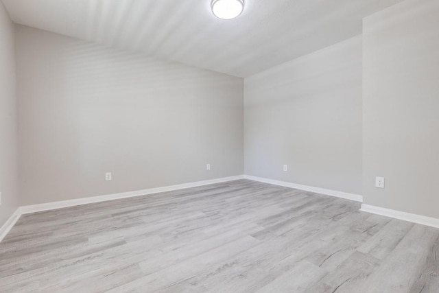 unfurnished room featuring baseboards, vaulted ceiling, and wood finished floors