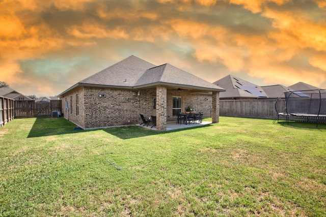 back of house with a fenced backyard, a lawn, a patio area, brick siding, and a trampoline