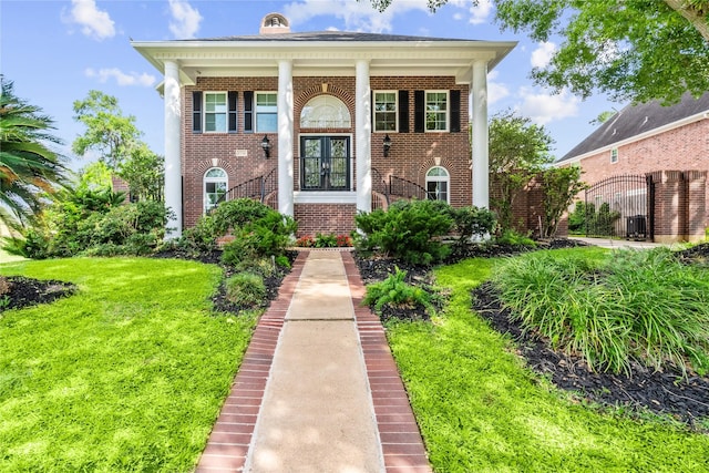 greek revival house featuring brick siding, french doors, and a front yard