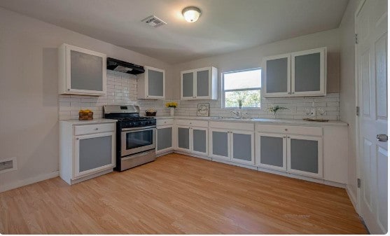 kitchen with light countertops, extractor fan, decorative backsplash, light wood finished floors, and stainless steel gas stove