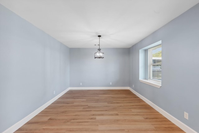 unfurnished dining area featuring baseboards, light wood-style floors, and an inviting chandelier