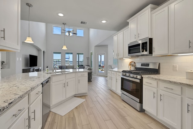 kitchen featuring stainless steel appliances, ceiling fan, a sink, open floor plan, and white cabinetry