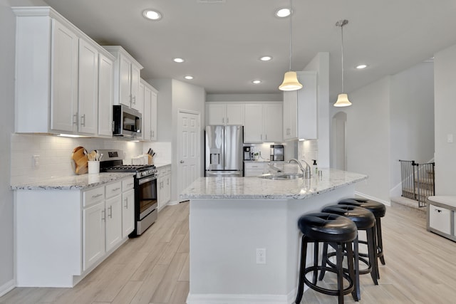 kitchen featuring stainless steel appliances, a sink, light wood finished floors, a kitchen bar, and white cabinets