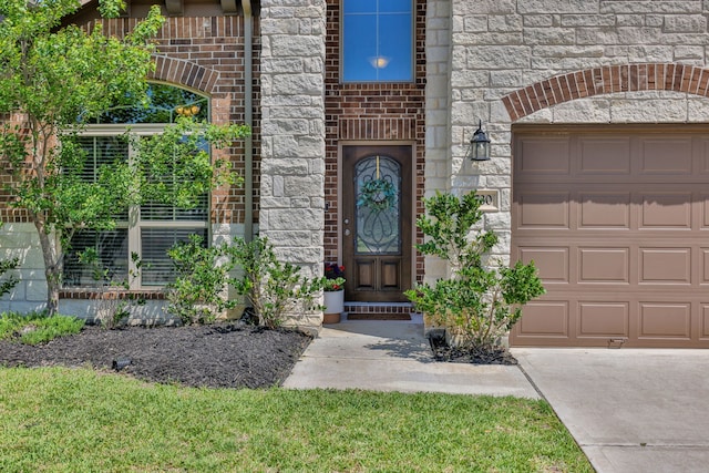 entrance to property featuring a garage, stone siding, brick siding, and driveway