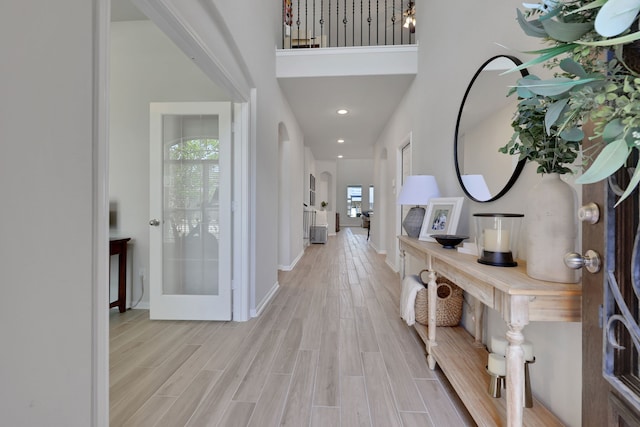 foyer featuring arched walkways, light wood-type flooring, a towering ceiling, baseboards, and recessed lighting