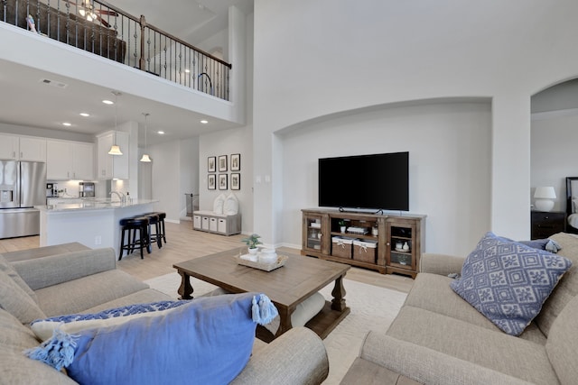 living area featuring light wood-style flooring, arched walkways, a towering ceiling, and recessed lighting