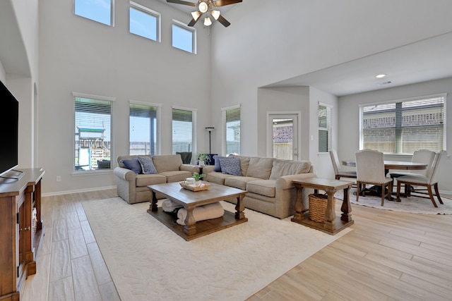 living room featuring a ceiling fan, healthy amount of natural light, wood finished floors, and a towering ceiling