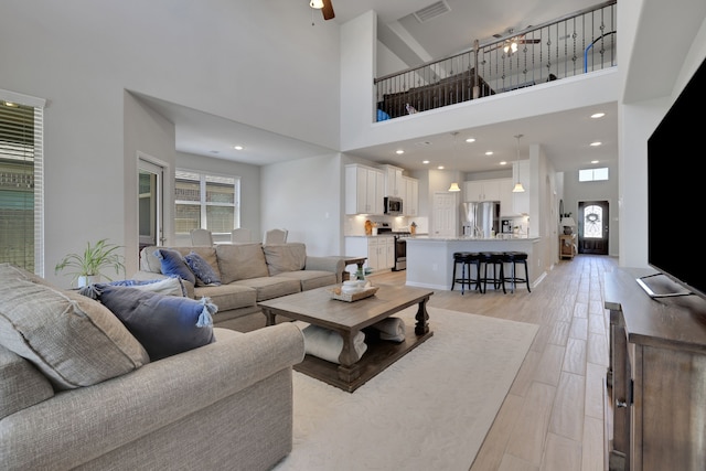 living area featuring a high ceiling, a ceiling fan, and light wood-style flooring