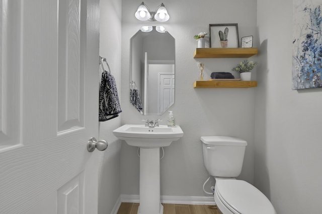 half bath featuring toilet, wood finished floors, baseboards, and a sink
