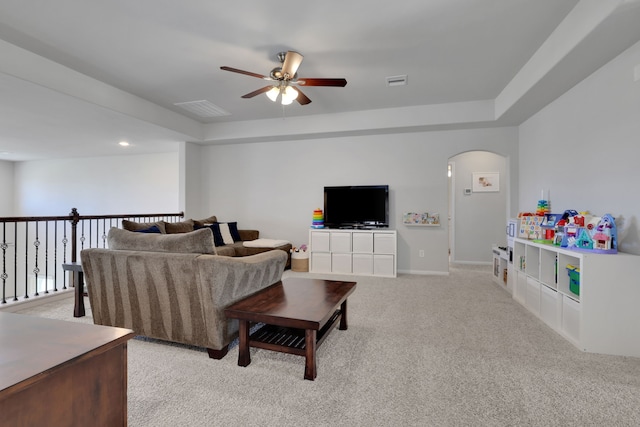 living room featuring a ceiling fan, arched walkways, light carpet, and baseboards