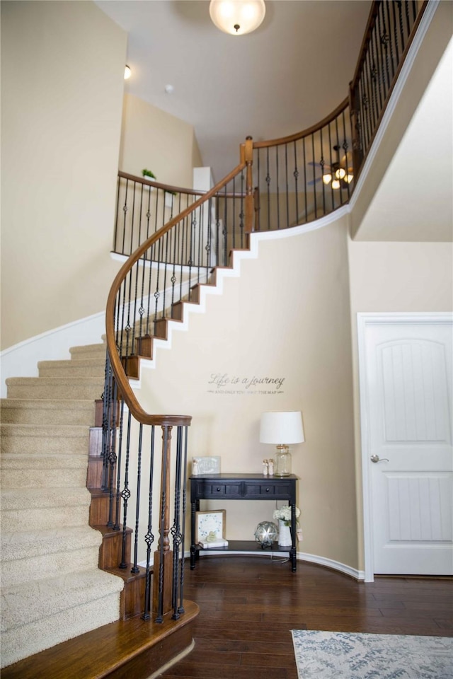 stairway featuring baseboards, a high ceiling, and wood finished floors