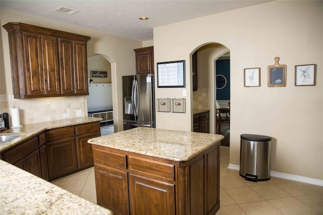 kitchen with backsplash, a center island, arched walkways, light tile patterned floors, and stainless steel fridge with ice dispenser