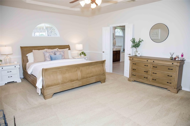 bedroom with ceiling fan, visible vents, a raised ceiling, connected bathroom, and light carpet