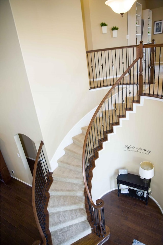 staircase with baseboards, arched walkways, and hardwood / wood-style flooring