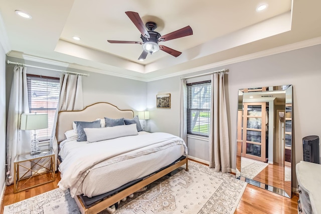 bedroom with ornamental molding, a tray ceiling, light wood-style flooring, and recessed lighting