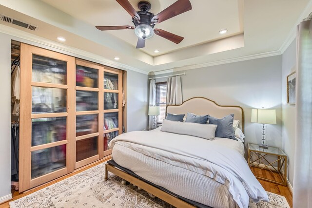 bedroom featuring visible vents, a tray ceiling, ornamental molding, and wood finished floors