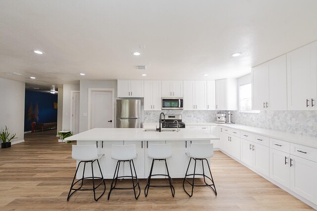 3718 Prudence Dr, Houston, TX 77045 - kitchen featuring tasteful backsplash, light wood-style floors, a center island with sink, a breakfast bar area, and stainless steel appliances