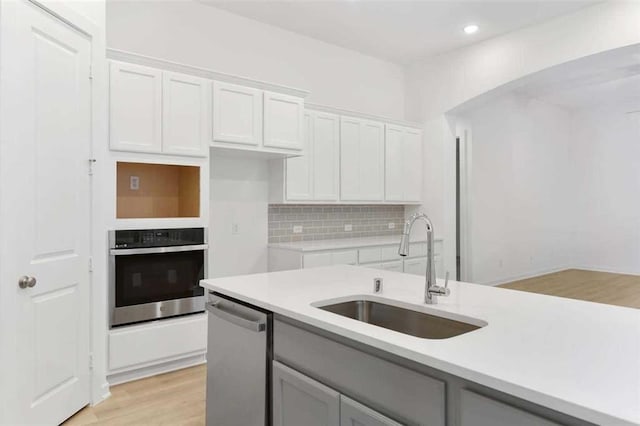 kitchen featuring light wood-style floors, white cabinets, a sink, stainless steel appliances, and decorative backsplash