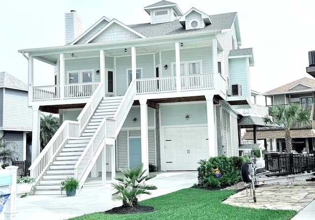 coastal inspired home with covered porch, a garage, a chimney, stairway, and driveway