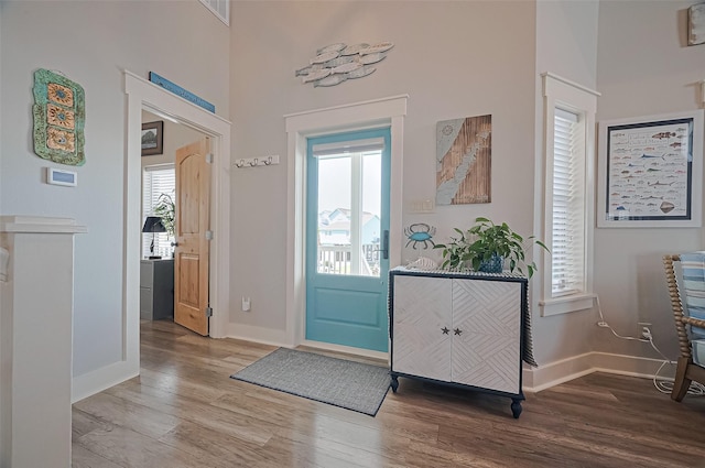 entrance foyer featuring wood finished floors, baseboards, visible vents, and a towering ceiling