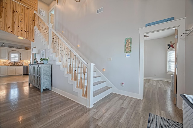 staircase with visible vents, a towering ceiling, wood finished floors, and a healthy amount of sunlight
