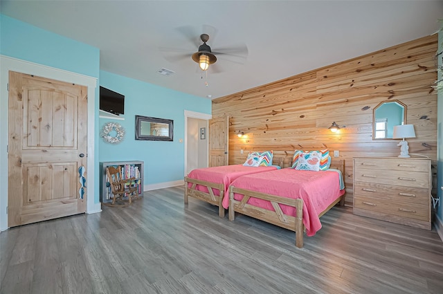 bedroom with a ceiling fan, visible vents, wood finished floors, wood walls, and baseboards