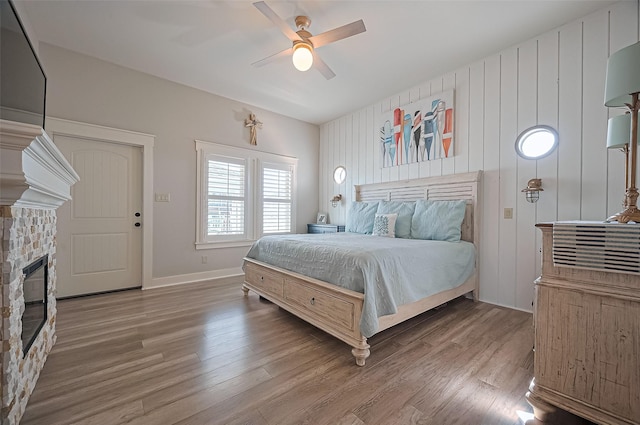bedroom featuring wood finished floors, ceiling fan, baseboards, and a stone fireplace