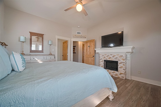 bedroom featuring a ceiling fan, a stone fireplace, visible vents, wood finished floors, and baseboards
