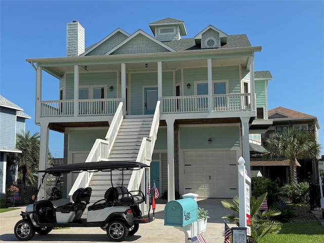 405 Amanda Cir, Tiki Island, TX 77554 - raised beach house with a garage, concrete driveway, a shingled roof, covered porch, and stairway
