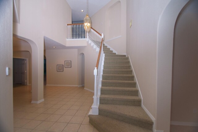 stairway featuring a chandelier, baseboards, arched walkways, tile patterned floors, and a high ceiling