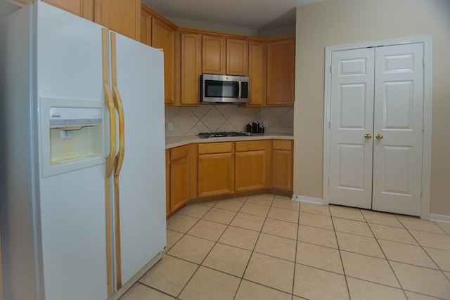 kitchen with stainless steel microwave, light tile patterned flooring, white fridge with ice dispenser, backsplash, and light countertops
