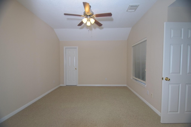 spare room featuring lofted ceiling, visible vents, baseboards, light carpet, and a ceiling fan