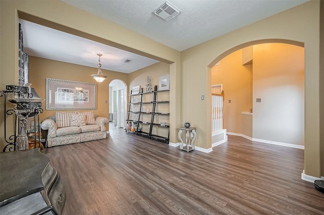 living area with arched walkways, baseboards, visible vents, and wood finished floors
