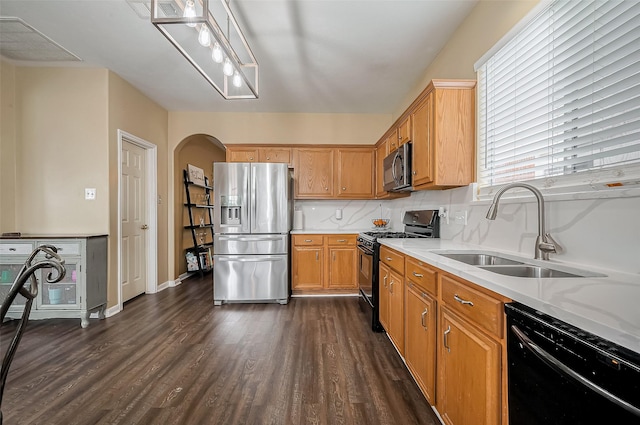 kitchen with brown cabinetry, arched walkways, a sink, black appliances, and dark wood-style floors