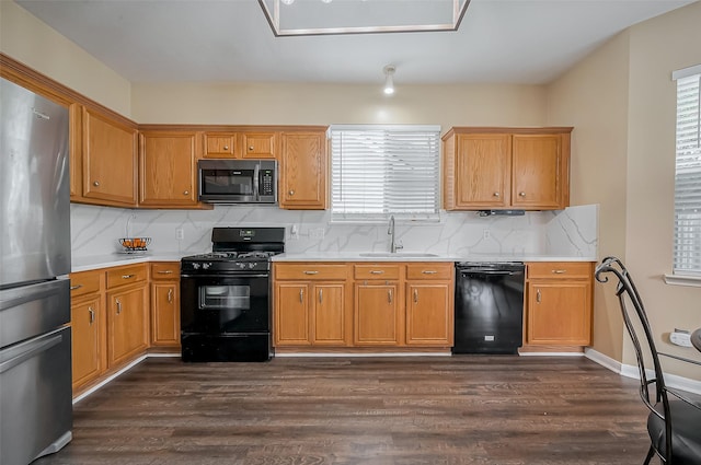 kitchen with dark wood-style flooring, a sink, light countertops, tasteful backsplash, and black appliances
