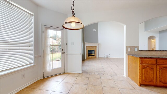 16410 Bluff Springs Dr, Houston, TX 77095 - kitchen with pendant lighting, light tile patterned floors, a fireplace, brown cabinetry, and arched walkways