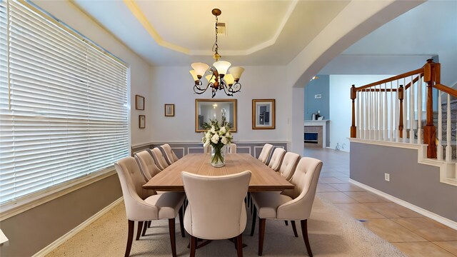 16410 Bluff Springs Dr, Houston, TX 77095 - tiled dining room featuring a fireplace, arched walkways, stairway, a raised ceiling, and a notable chandelier