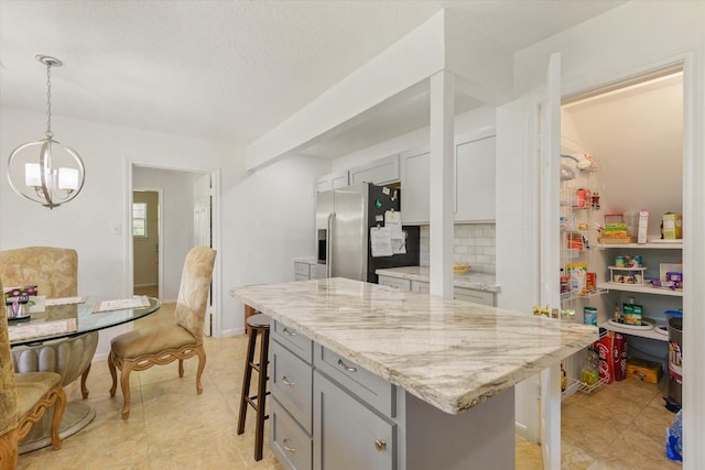 kitchen featuring stainless steel refrigerator with ice dispenser, an inviting chandelier, a breakfast bar area, gray cabinetry, and light stone counters