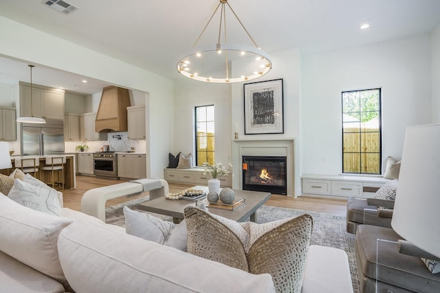 living area with a wealth of natural light, light wood-style floors, visible vents, and a chandelier