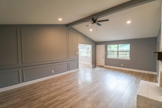 unfurnished living room with ceiling fan, a brick fireplace, wood finished floors, baseboards, and vaulted ceiling with beams