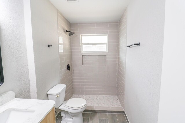 full bath featuring vanity, visible vents, wood finished floors, toilet, and a tile shower