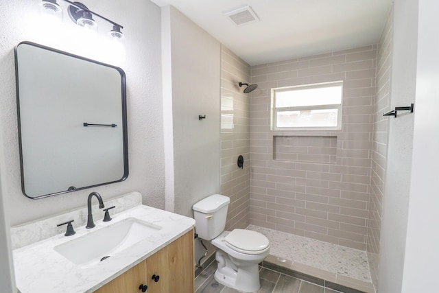 bathroom with vanity, a tile shower, toilet, and visible vents