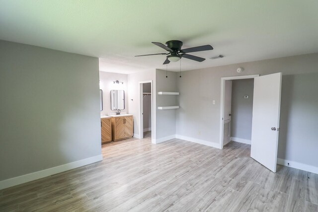 interior space with a sink, baseboards, a spacious closet, light wood-type flooring, and visible vents