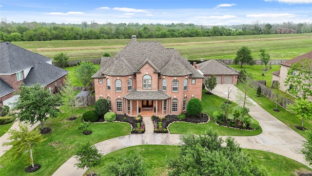 view of front facade featuring a chimney, driveway, brick siding, fence, and a shingled roof