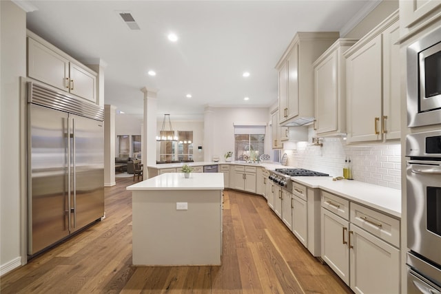 kitchen with backsplash, light wood-style floors, built in appliances, and visible vents