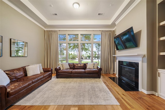 living area with visible vents, a raised ceiling, a tile fireplace, and wood finished floors